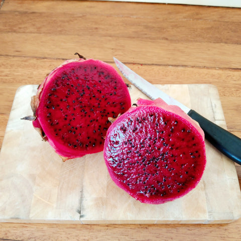 A pink dragonfruit cut in half, showing the vibrant flesh and small black seeds.